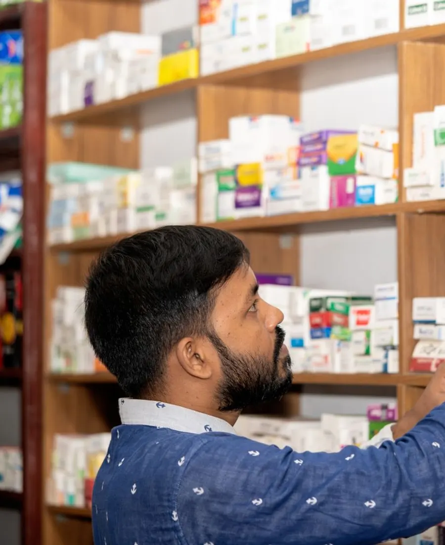 A pharmacist taking a medicine box down from a stocked shelf